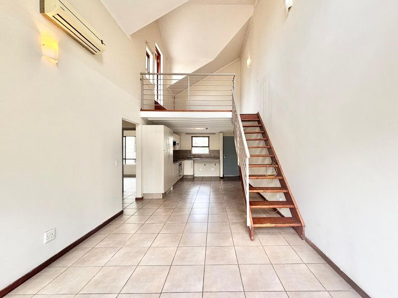 Spacious open-plan living area featuring a mezzanine level, wooden staircase, tiled flooring, and a functional kitchen with built-in cabinetry and appliances.