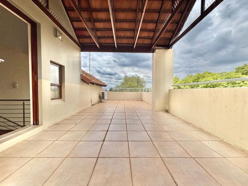 Spacious covered balcony featuring tiled flooring, a timber roof structure, and metal balustrades, offering an open outdoor area suitable for relaxation.