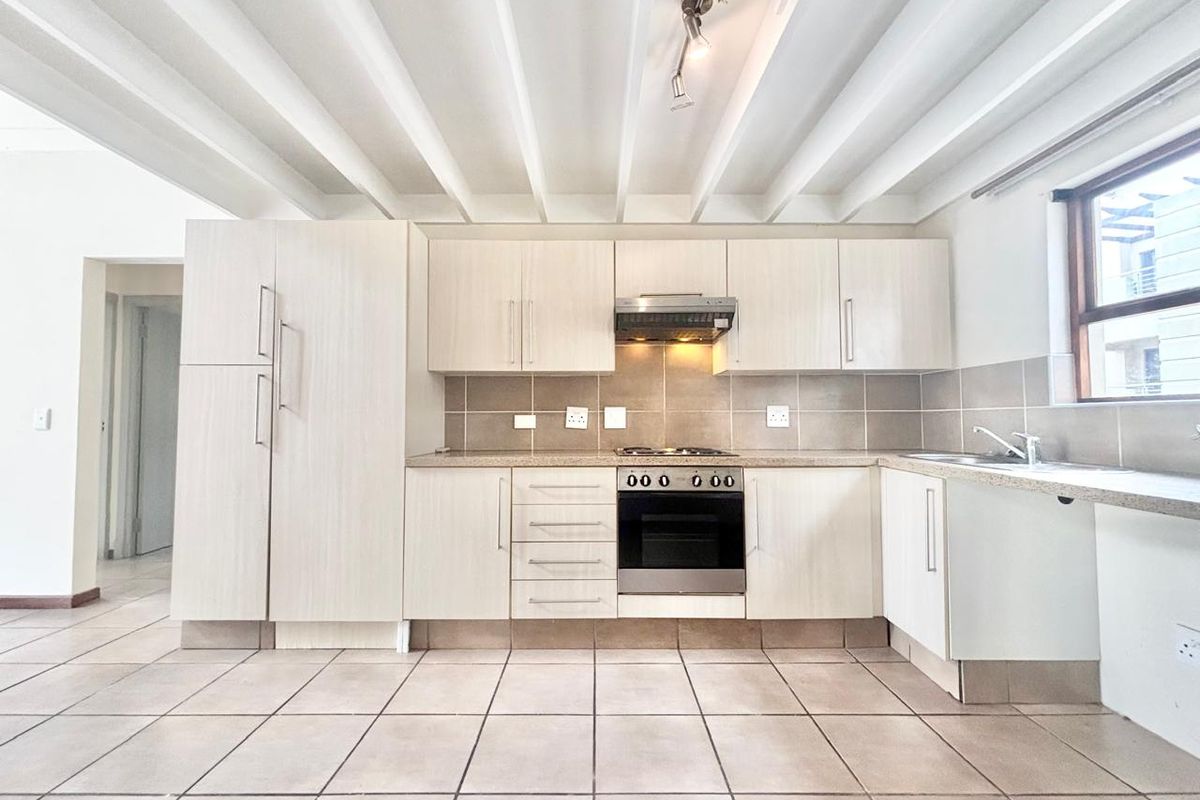 A clean, functional kitchen featuring light wood-finish cabinetry, tiled flooring, built-in oven and hob, and an exposed beam ceiling.