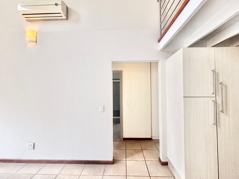 An empty living area featuring tiled flooring, a split-system air conditioner, built-in storage cabinetry, and a mezzanine level overlooking the space.