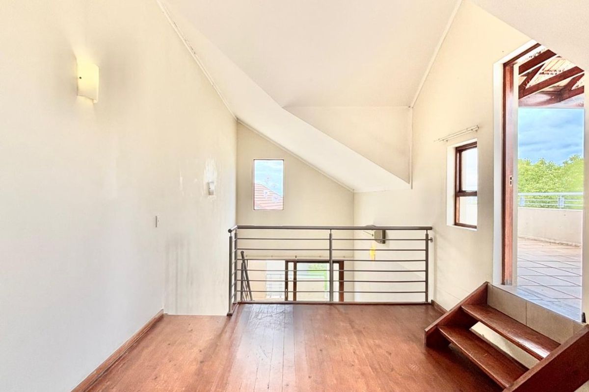 An empty, light-filled loft area featuring hardwood flooring, a vaulted ceiling, and a metal balustrade, with direct access to an outdoor balcony.