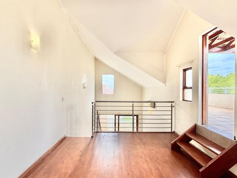 An empty, light-filled loft area featuring hardwood flooring, a vaulted ceiling, and a metal balustrade, with direct access to an outdoor balcony.