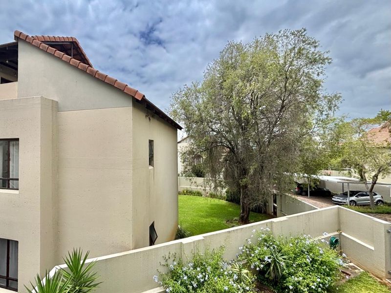 A view of the rear exterior of the apartment building, featuring a landscaped garden, boundary wall, and a covered carport area.