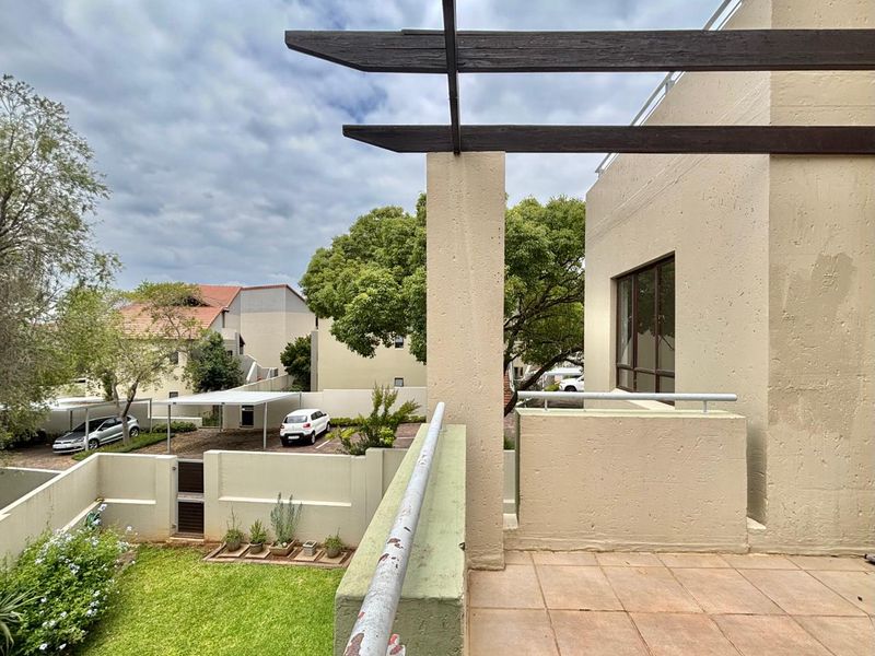 An elevated balcony featuring a timber pergola, tiled flooring, and a metal balustrade overlooking the complex grounds.
