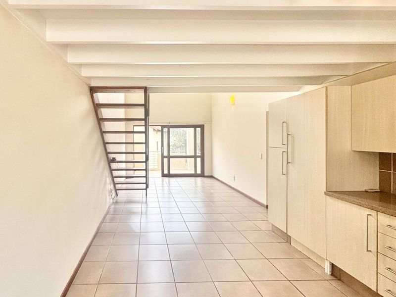 An open-plan living and kitchen area featuring tiled floors, exposed ceiling beams, built-in cabinetry, and a staircase leading to an upper level.