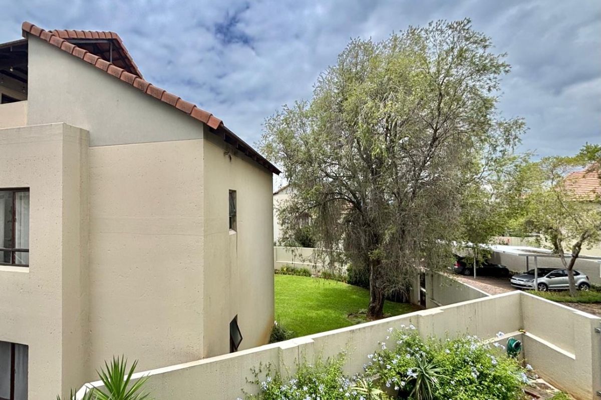 A view of the rear exterior of the apartment building, featuring a landscaped garden, boundary wall, and a covered carport area.