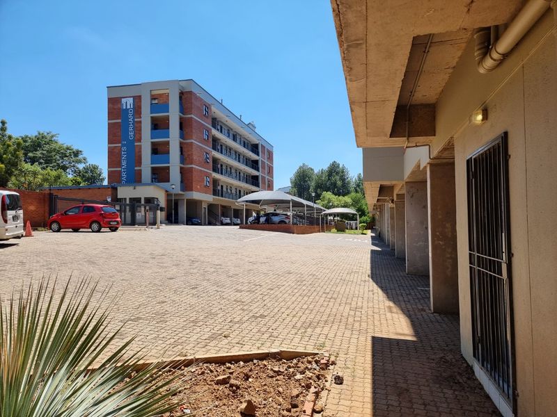Exterior view of the apartment complex featuring a paved parking area, covered parking bays, and brick building facade.