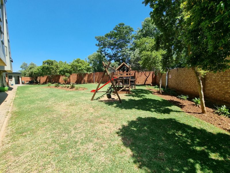 A spacious communal garden area featuring a well-maintained lawn, mature trees, and secure brick boundary walls.