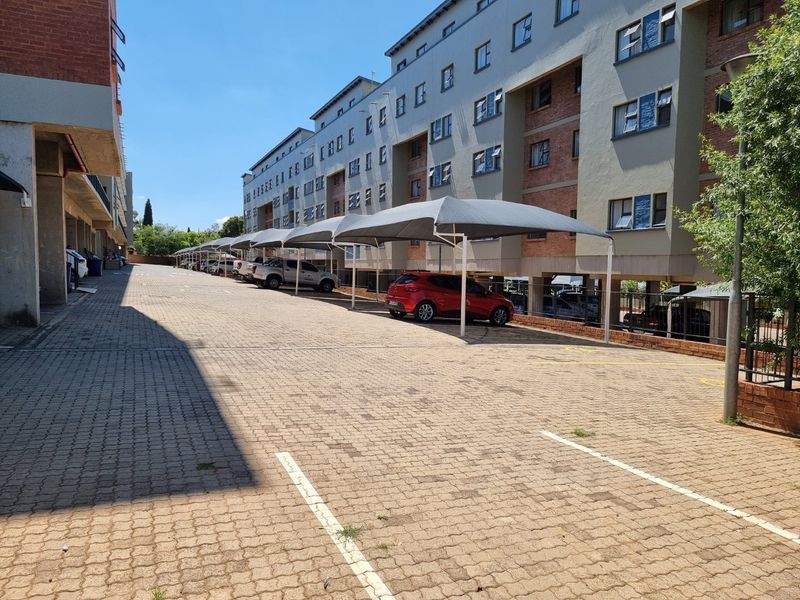 Exterior view of the apartment complex featuring a paved parking area with covered carports and multi-story residential building facade.