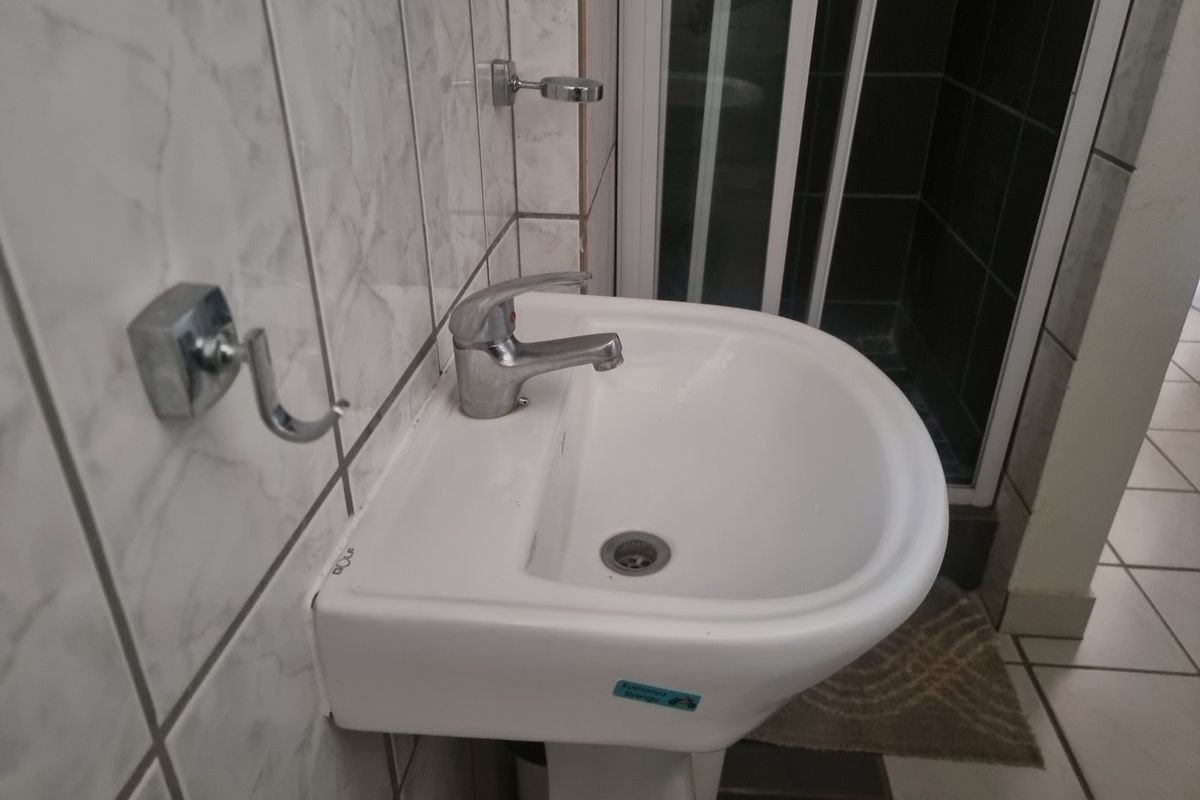 A functional bathroom featuring a pedestal washbasin with a chrome mixer tap, tiled wall finishes, and a separate shower enclosure.