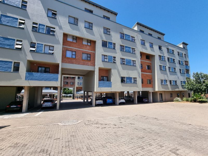 Exterior view of a multi-story apartment complex featuring a paved driveway and integrated covered parking bays.