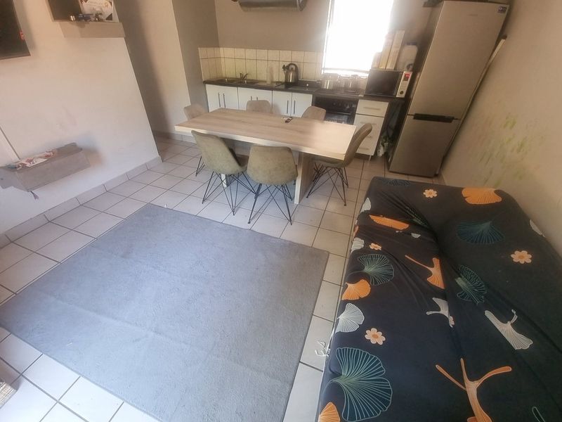 Open plan living and kitchen area featuring tiled flooring, functional cabinetry, and a tiled backsplash, requiring cosmetic updates to the walls.