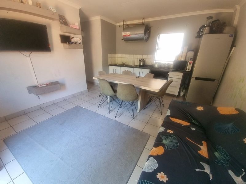 Open-plan living and kitchen area featuring tiled flooring, wall-mounted geyser, and basic cabinetry, offering potential for modernization and improved layout.