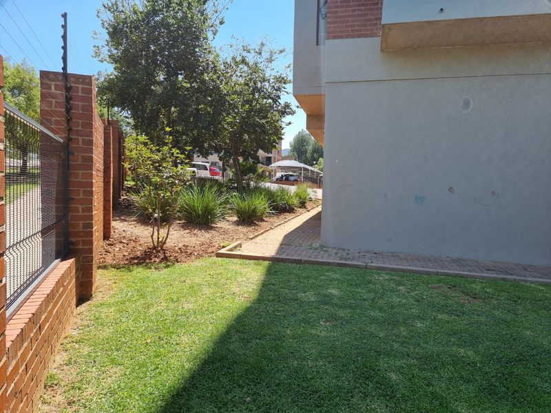 A view of the rear exterior area featuring a manicured lawn, paved walkway, and a brick boundary wall with electric fencing.