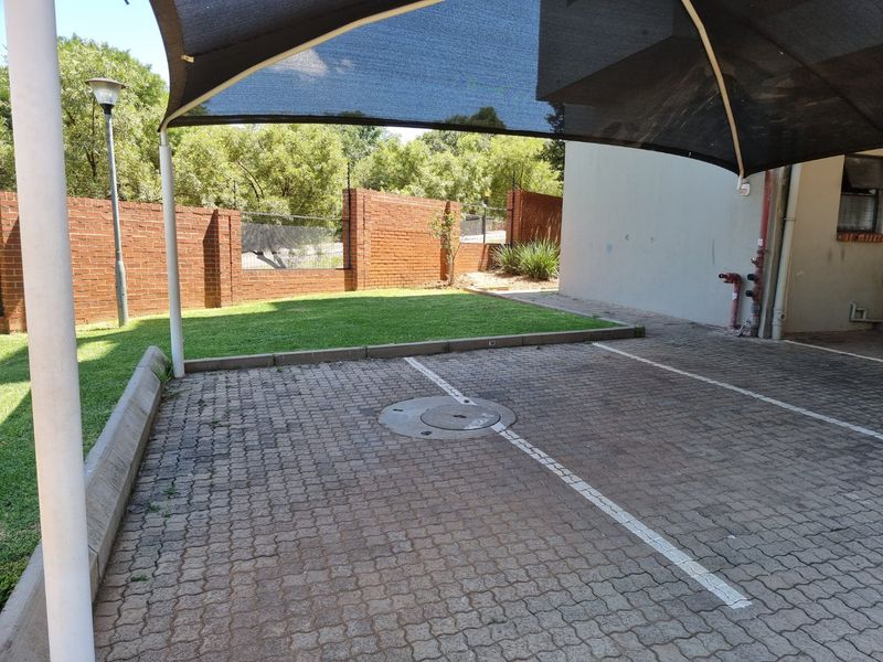 A paved parking area featuring a shade sail, brick boundary wall, and small lawn area, providing dedicated outdoor parking space for the apartment.