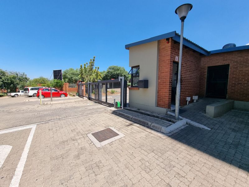 Exterior view of the apartment complex entrance featuring a security gate, guard house, and paved driveway area.