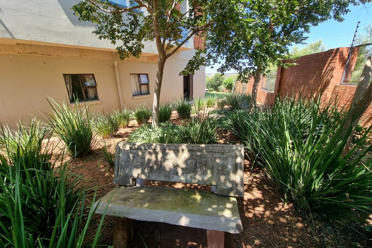 A rear garden area featuring established landscaping, a concrete bench, and a brick boundary wall with integrated electric fencing.