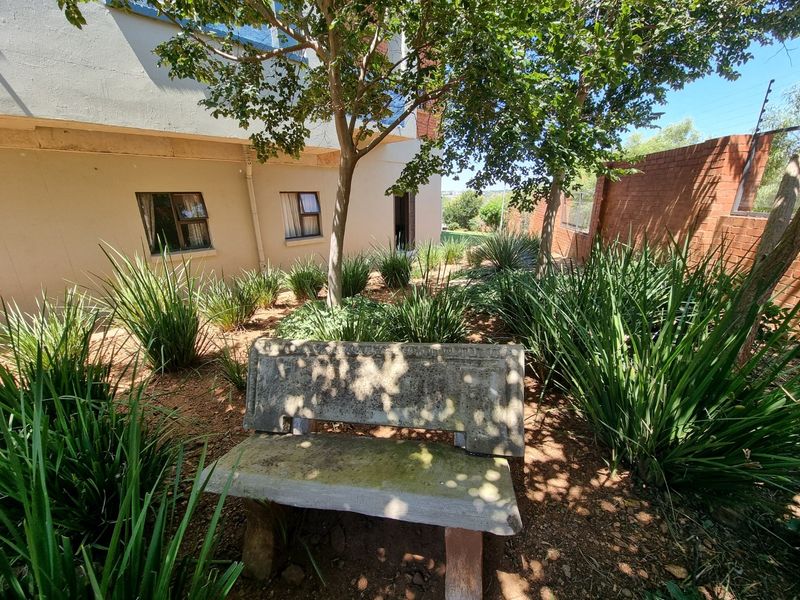 A rear garden area featuring established landscaping, a concrete bench, and a brick boundary wall with integrated electric fencing.