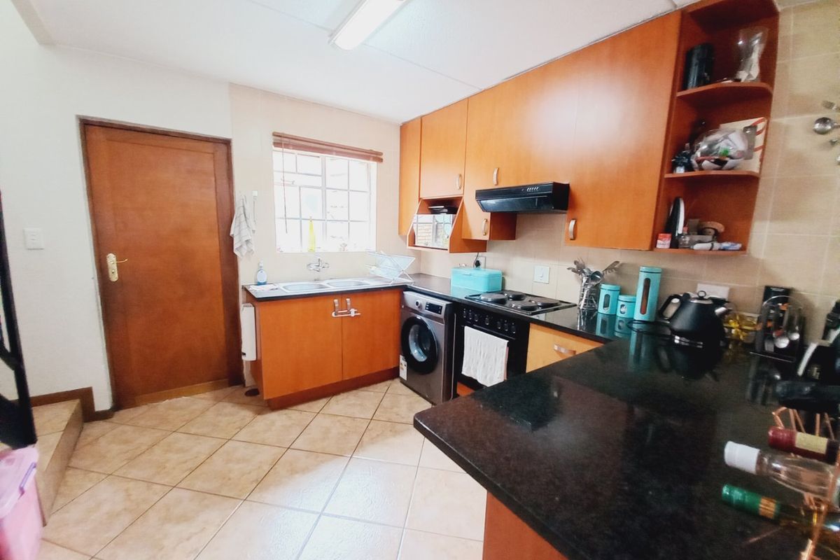 Functional kitchen featuring wooden cabinetry, dark granite countertops, built-in oven with extractor fan, and tiled flooring with direct access to an adjacent area.