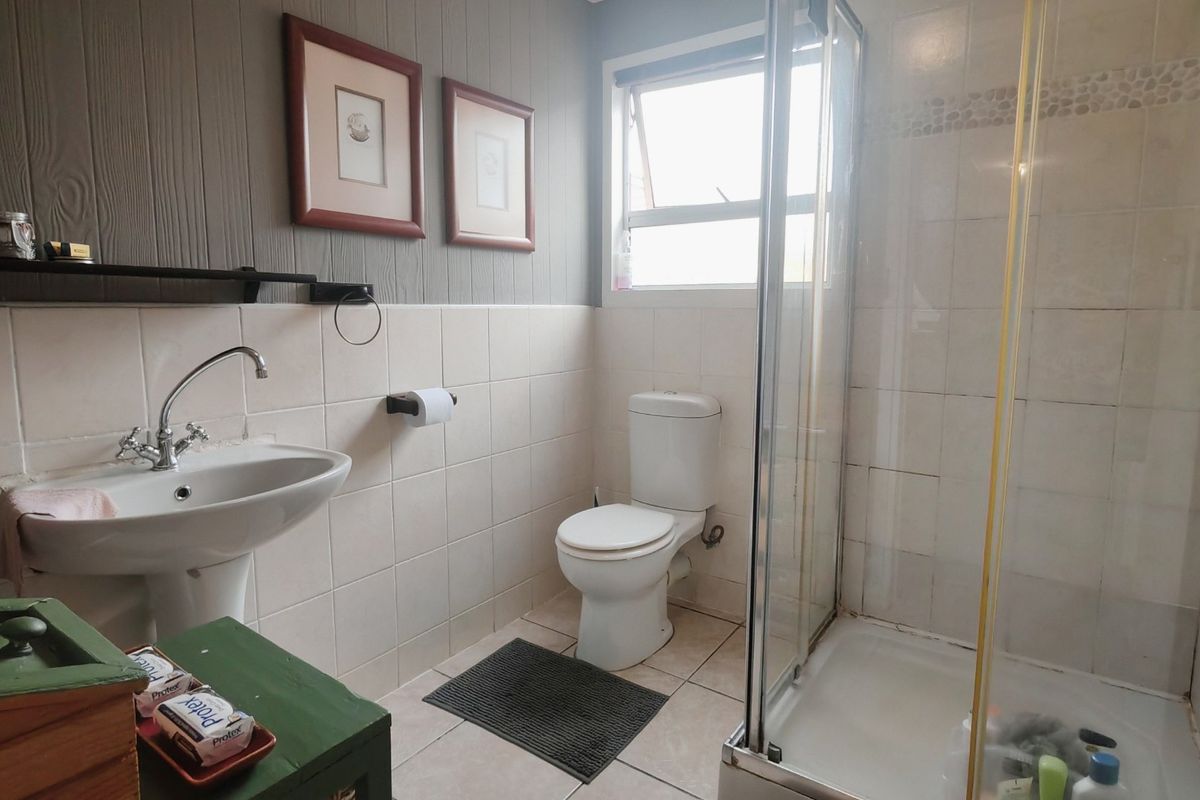 A functional bathroom featuring a pedestal basin, toilet, and a glass-enclosed shower with tiled walls and flooring.