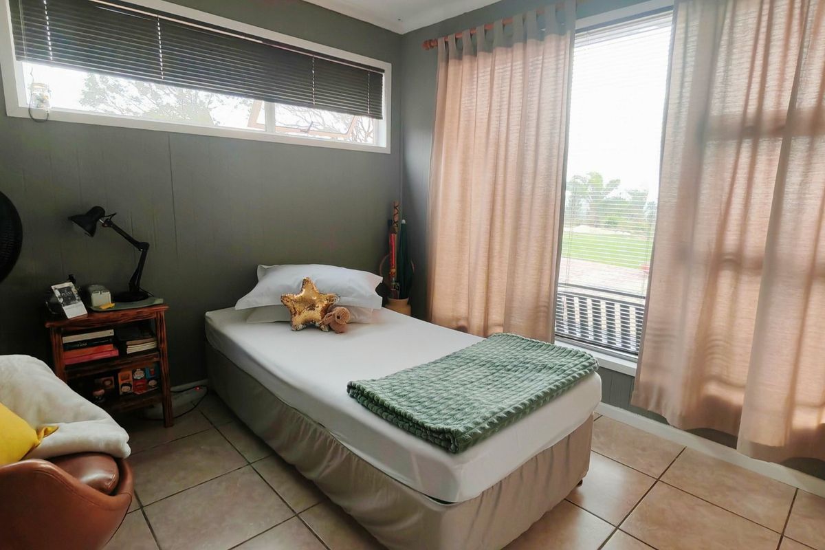 A bedroom featuring tiled flooring, large windows with blinds and curtains, providing natural light and a view of the exterior grounds.