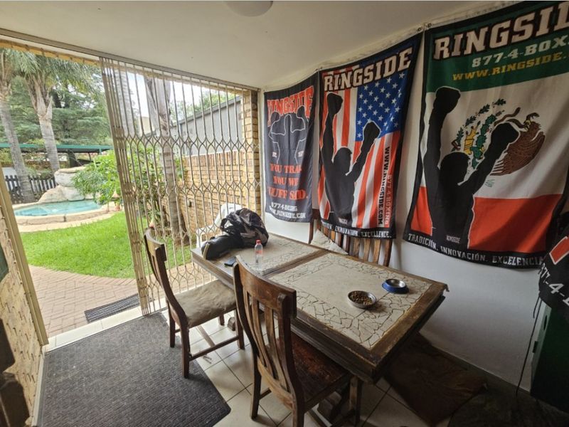 A covered patio area featuring tiled flooring and a security gate, providing direct access to the garden and pool area.