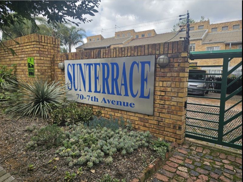 Front entrance view of Sunterrace complex, featuring a brick boundary wall, electric fencing, and secure metal gate access.