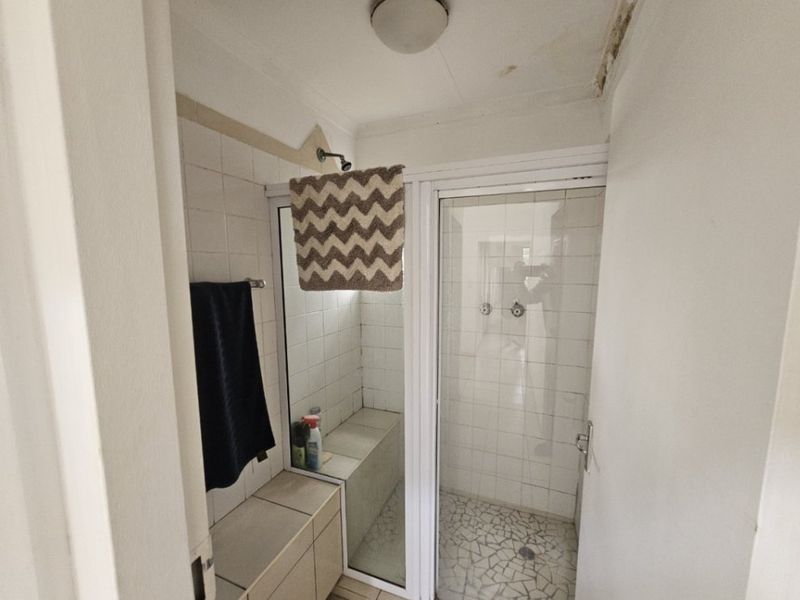A functional bathroom shower area featuring a built-in bench, tiled walls, and a mosaic floor, currently showing signs of ceiling water damage.