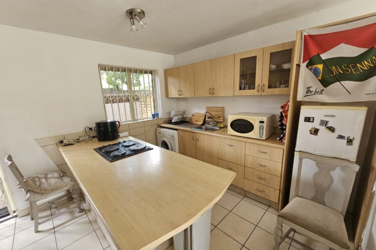 Functional kitchen featuring light wood-finish cabinetry, laminate countertops with an integrated hob, tiled flooring, and a window with security bars.