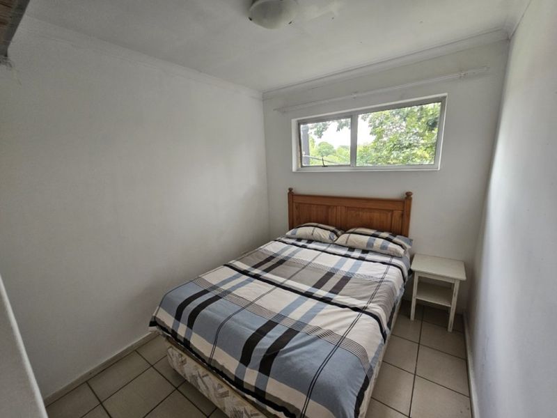A compact bedroom featuring tiled flooring and a sliding window, offering a functional space ready for cosmetic updates.