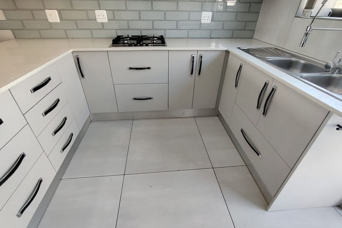Modern kitchen featuring light grey cabinetry, quartz countertops, a gas hob, subway tile backsplash, and a double bowl stainless steel sink.