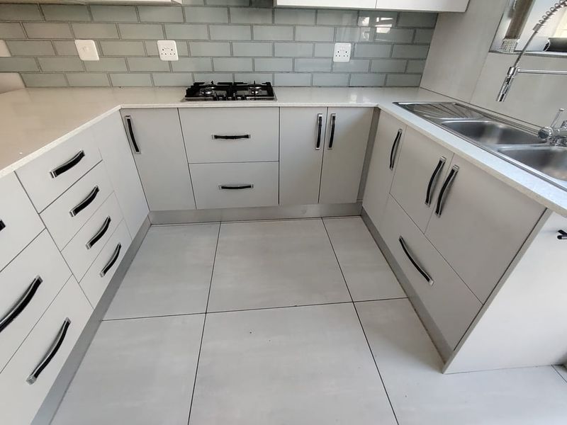 Modern kitchen featuring light grey cabinetry, quartz countertops, a gas hob, subway tile backsplash, and a double bowl stainless steel sink.