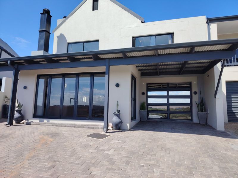 Modern front elevation featuring a paved driveway, covered patio area, large glass sliding doors, and a contemporary garage door.