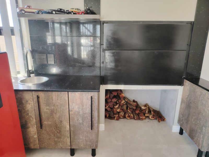 A modern built-in braai area featuring a sleek black granite countertop, integrated sink, and dedicated wood storage compartment.