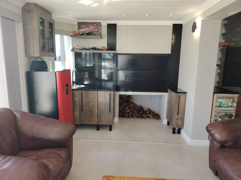 A well-appointed living area featuring a built-in braai, integrated kitchenette with granite countertops, and modern cabinetry, creating a functional entertainment space.