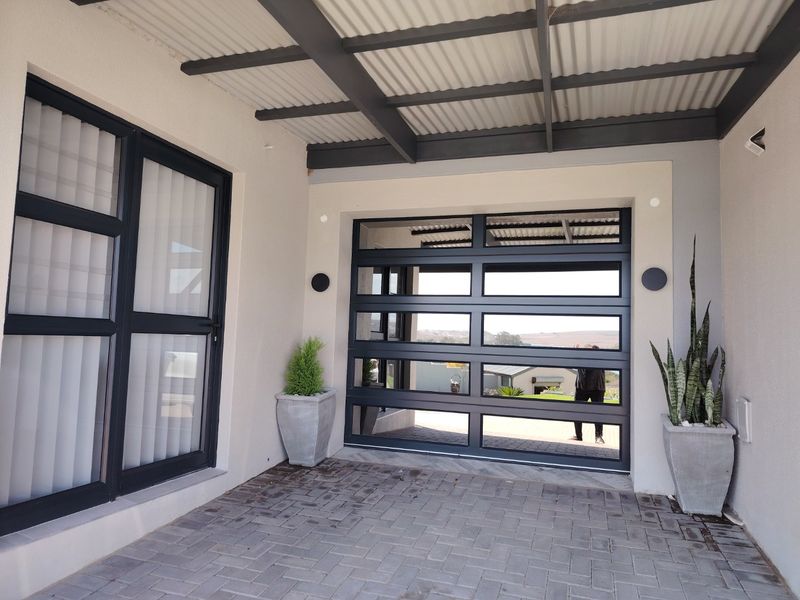 A modern covered patio area featuring paved flooring, a corrugated metal roof, and a contemporary glass-panelled garage door.