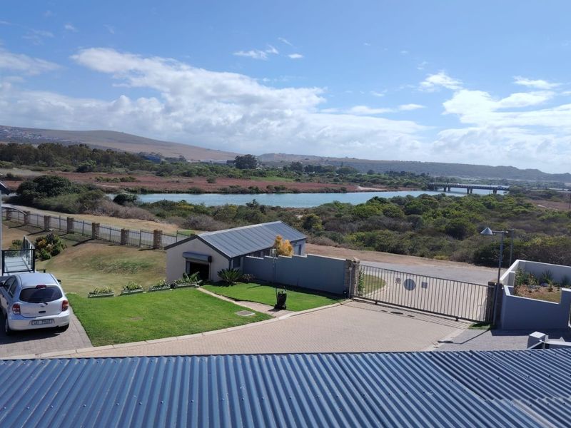 Elevated view overlooking the property grounds, featuring a paved driveway, metal gate, outbuilding, and scenic landscape with a river and bridge in the distance.