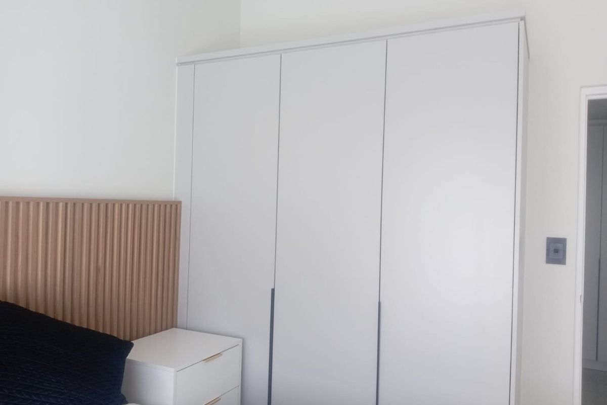 A modern bedroom featuring a floor-to-ceiling built-in wardrobe and a decorative slatted timber headboard.