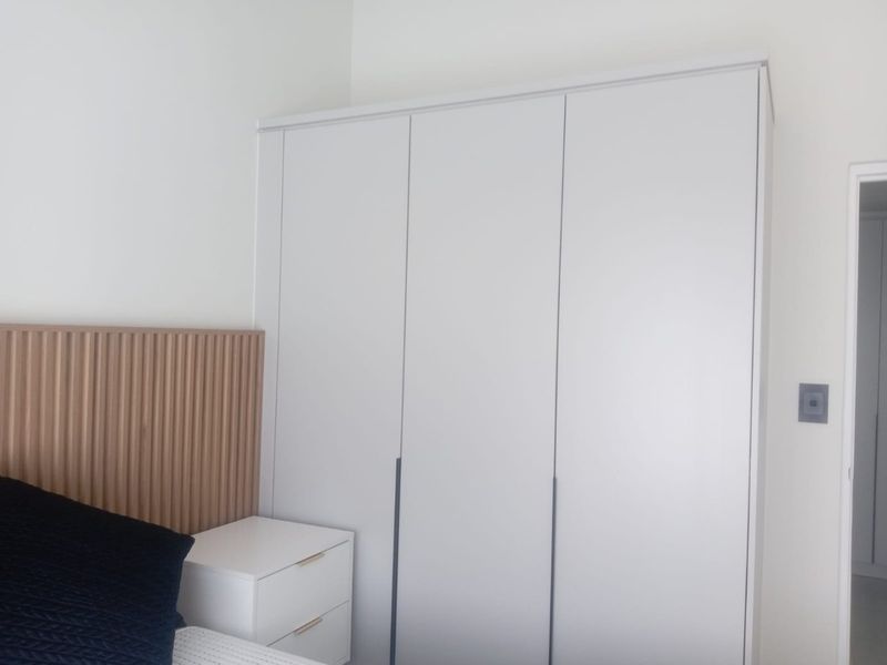 A modern bedroom featuring a floor-to-ceiling built-in wardrobe and a decorative slatted timber headboard.