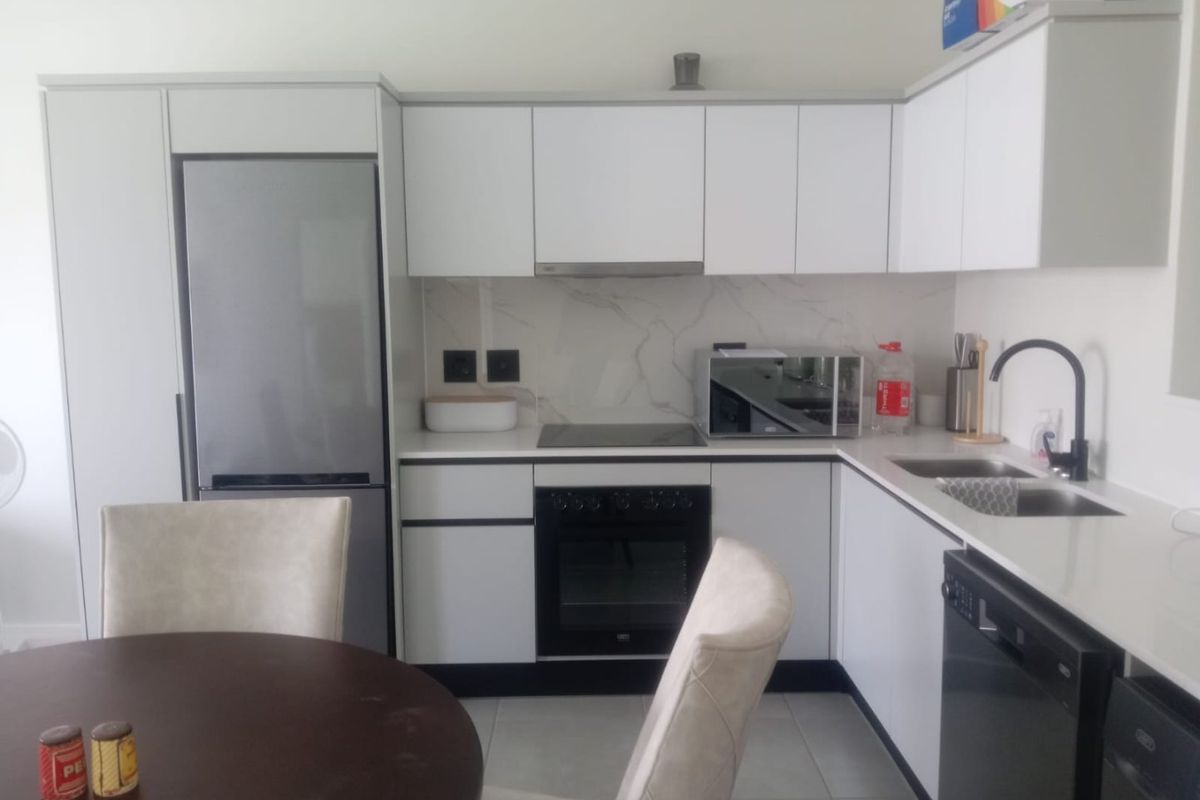 Modern kitchen featuring white cabinetry, stone countertops, marble-look splashback, integrated appliances, and a sleek black mixer tap.