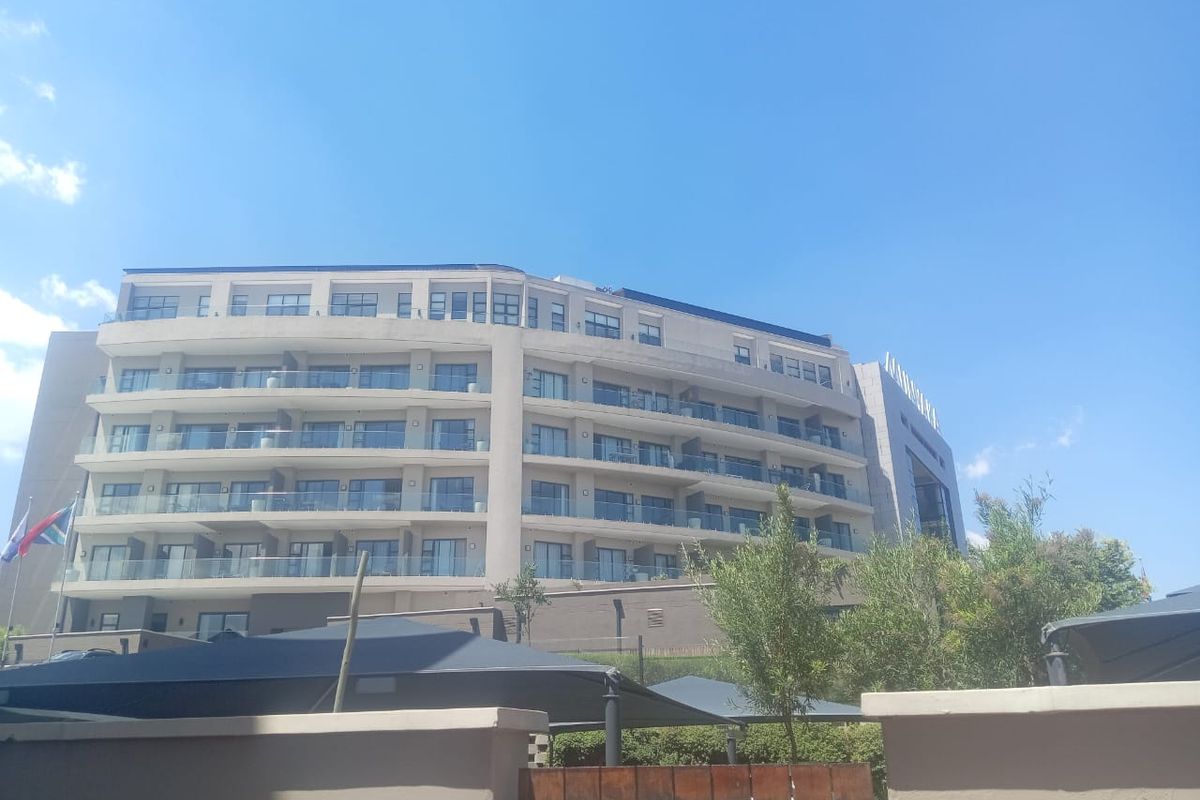 A view of the rear elevation of a modern multi-story apartment building featuring glass-fronted balconies and a contemporary concrete facade.