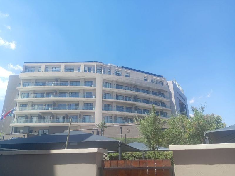 A view of the rear elevation of a modern multi-story apartment building featuring glass-fronted balconies and a contemporary concrete facade.