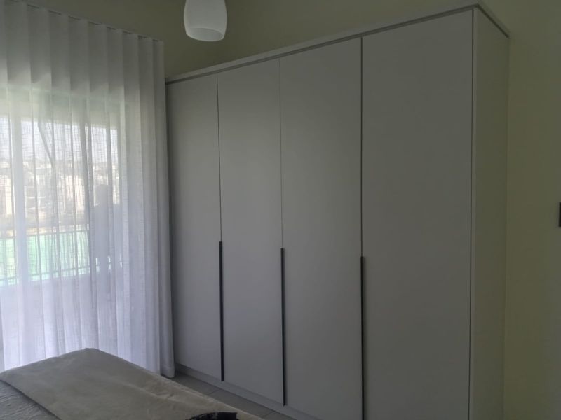 A bedroom featuring a modern, full-height built-in wardrobe with sleek vertical handles and floor-to-ceiling window treatments.