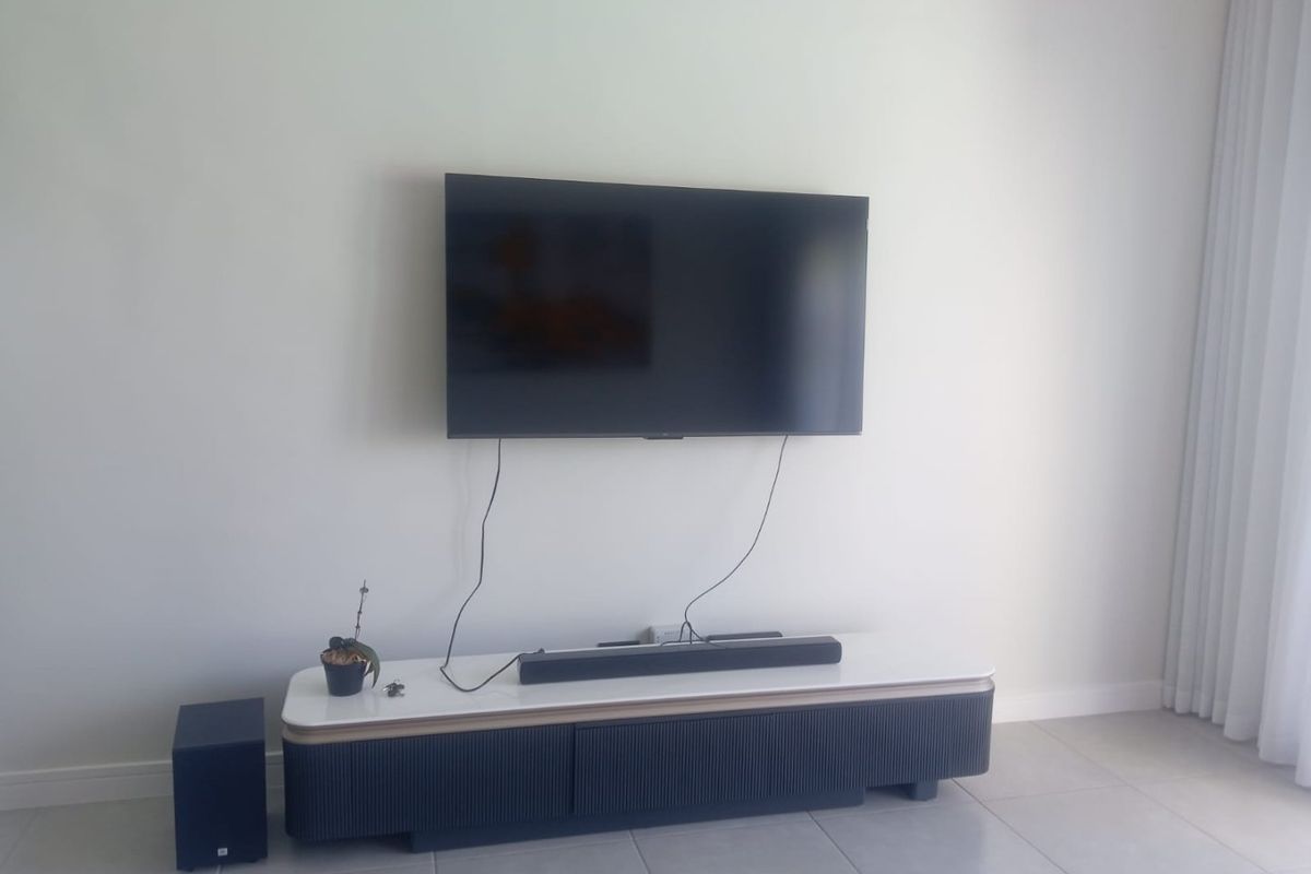 A bright living room area featuring neutral tiled flooring and wall-mounted television setup.