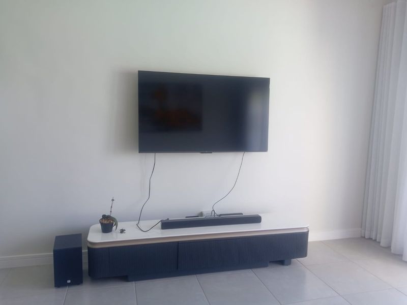 A bright living room area featuring neutral tiled flooring and wall-mounted television setup.