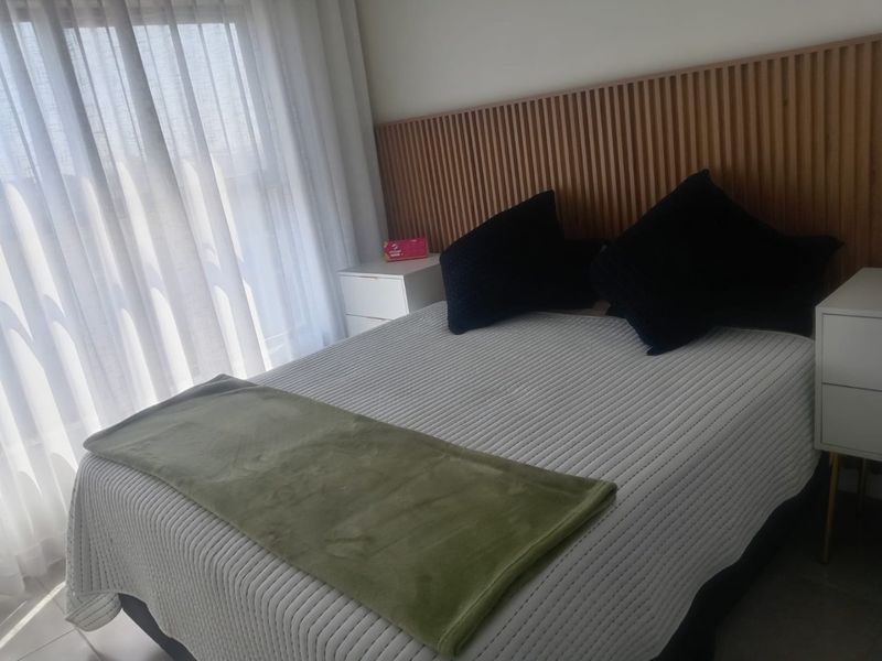 A well-maintained bedroom featuring a modern timber slat feature wall and floor-to-ceiling sheer curtains, providing a clean and contemporary aesthetic.