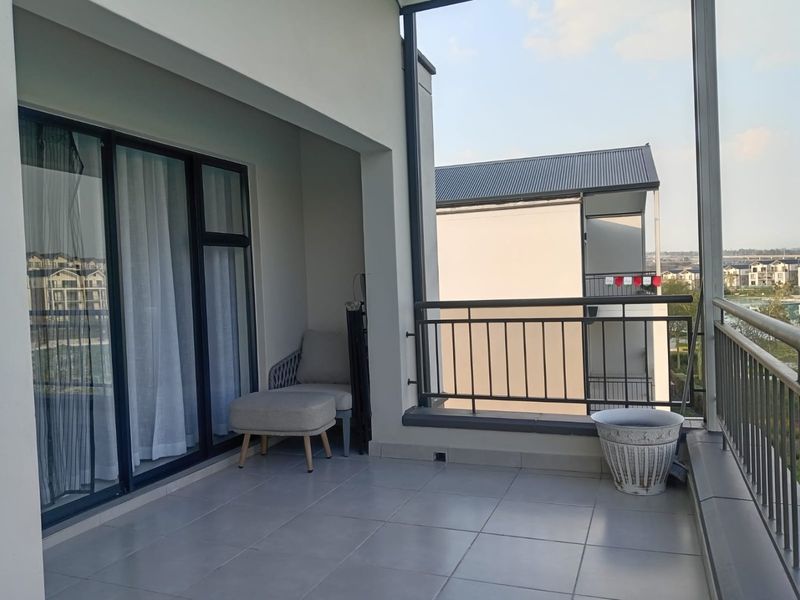A spacious covered balcony featuring tiled flooring and a metal balustrade, offering an open outdoor area accessible through sliding glass doors.