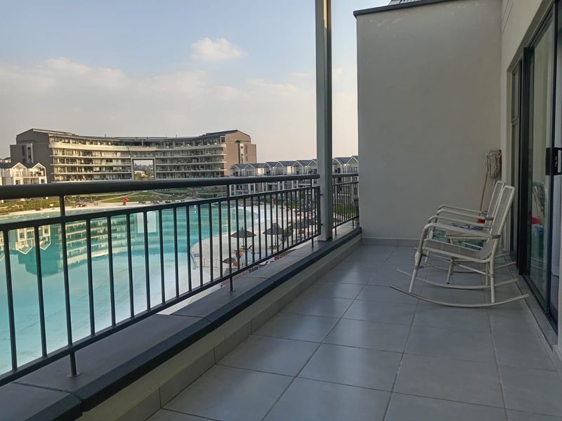 A spacious covered balcony featuring tiled flooring and a metal balustrade, offering clear views of the complex pool and surrounding residential architecture.