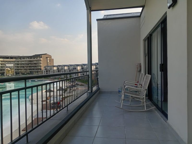 A spacious covered balcony featuring tiled flooring, a metal balustrade, and sliding glass doors, offering views of the estate pool area.