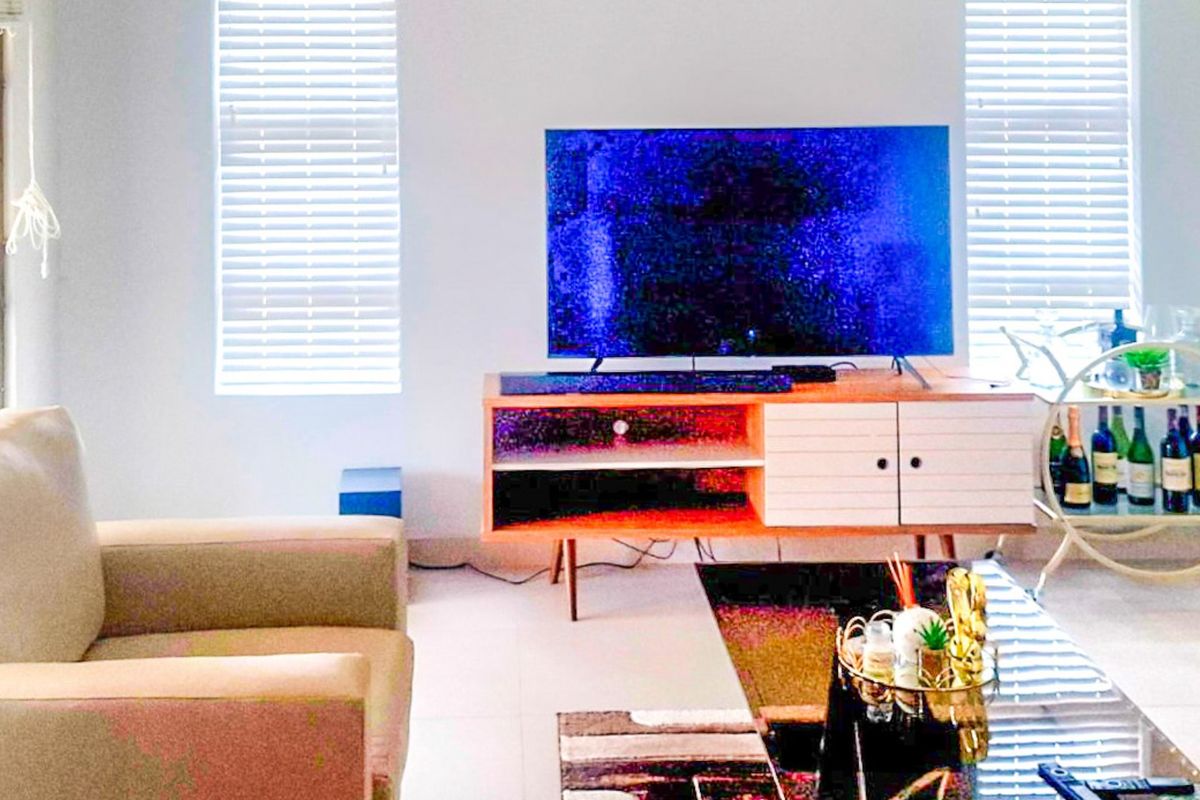 A bright living room featuring tiled flooring and dual windows fitted with venetian blinds.